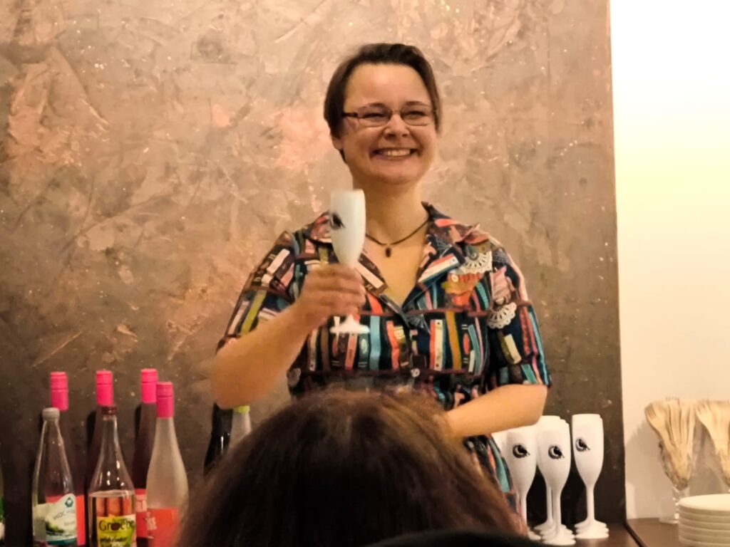 Sissi strahlt mit einem Glas Sekt in ihrem Bücherkleid in die Gästeschar.
